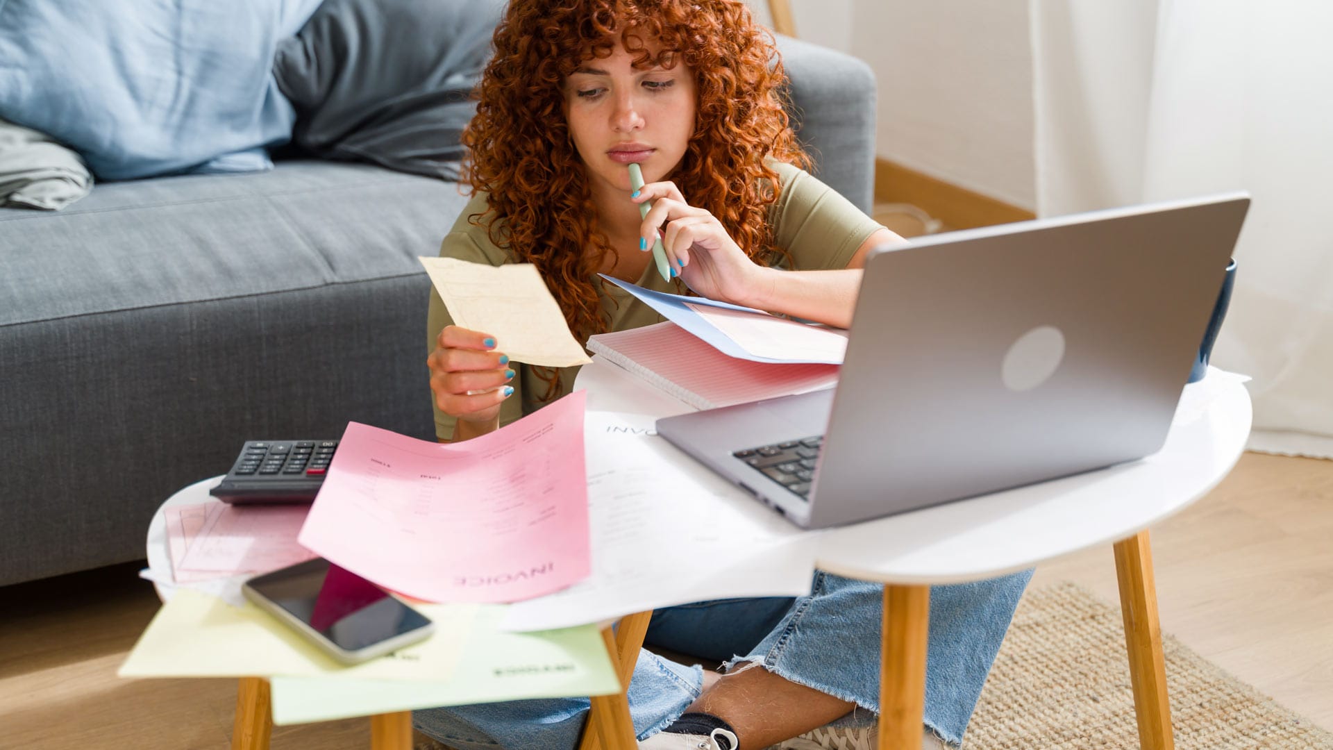 Nuori nainen tekee laskelmia säästöistään paperien, laskimen ja tietokoneen avulla.